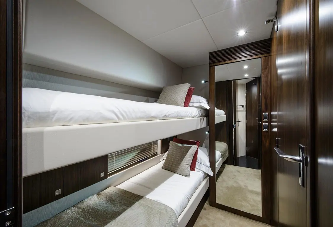 Bunk beds in a stylish cabin with decorative pillows, mirrored wardrobe, and modern lighting, featuring soft tones and textures.